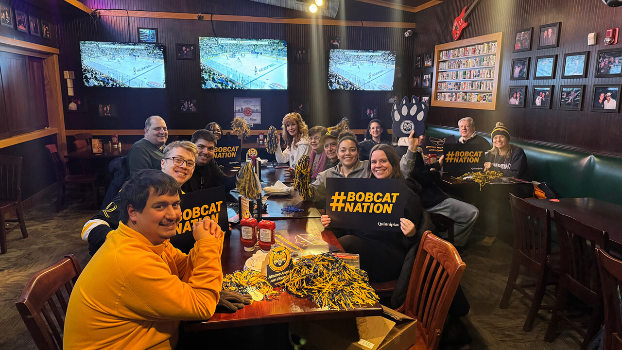 Alumni cheer on Quinnipiac men's ice hockey at a reception.
