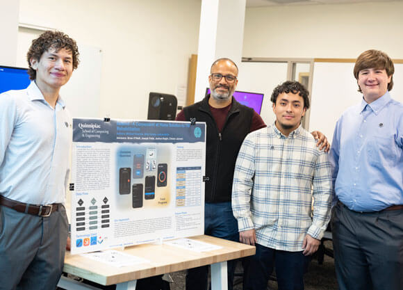 Michael Alvarado, Billy Godoy and Joshua Molin stand with faculty mentor Chetan Jaiswal beside a presentation display for ReMind, an iOS app designed to support concussion and mild traumatic brain injury recovery through cognitive exercises, symptom tracking and progress monitoring.