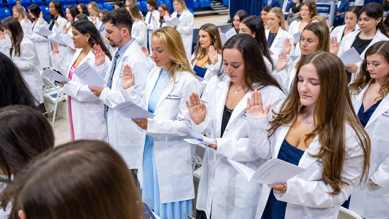 Dozens of Quinnipiac physician assistants in their white coats hold up their hands to say an oath
