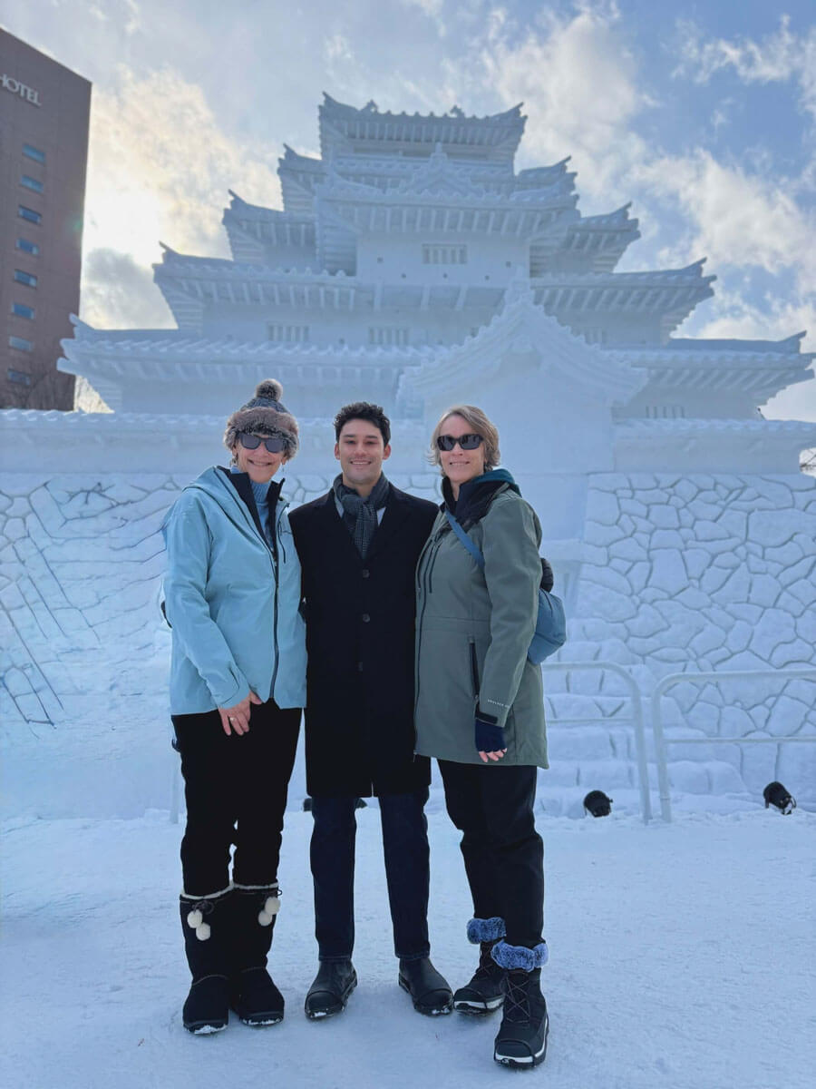 Three Quinnipiac alums in winter coats pose for a photo in front of an ice sculpture