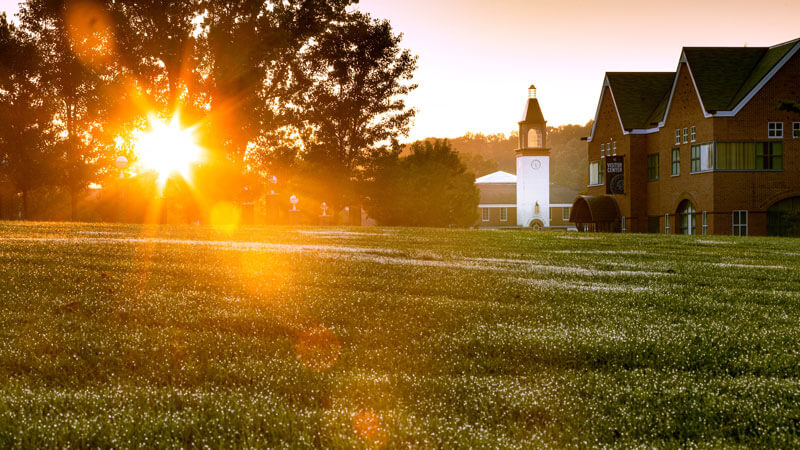 Sunrise over the grassy quad with the Quinnipiac library tower in the distance