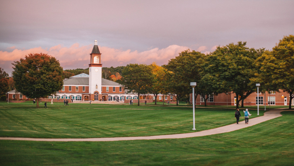 Students walk down a path on the quad with the Arnold Bernhard Library in the distance under a twilight pink sky