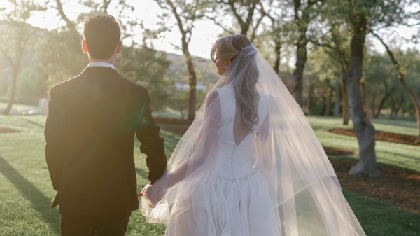 Two people holding hands and looking into the distance, one wearing a suit and the other a wedding dress