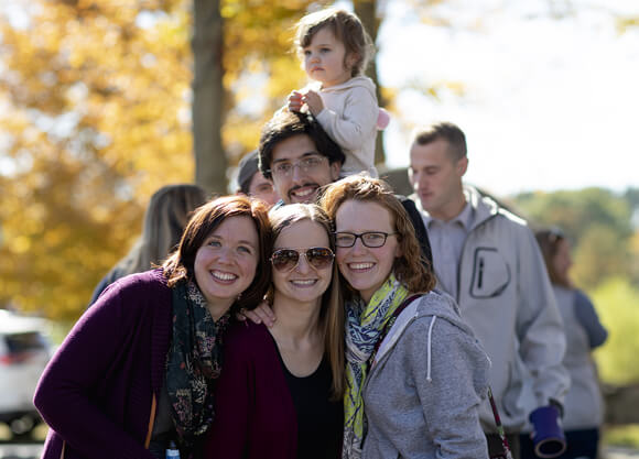 An alumni family of multiple generations smile for a photo on a fall day