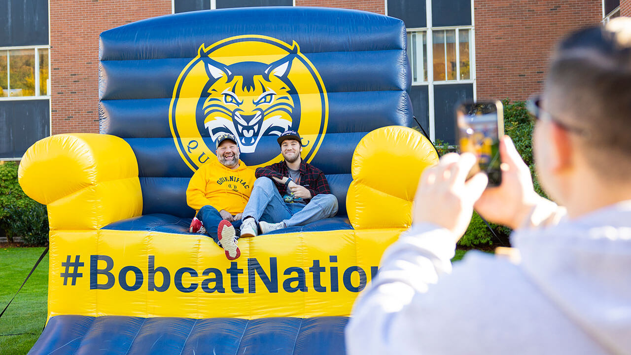 Bobcats smile for a photo on a giant Quinnipiac chair.