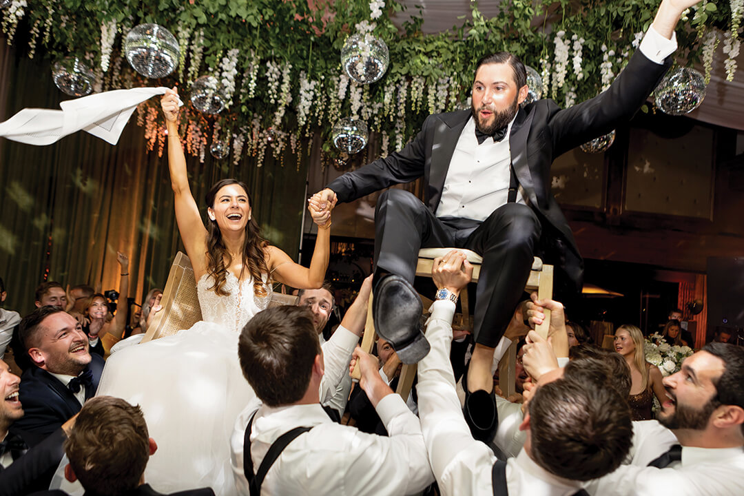 Alex Leafer and wife are lifted on chairs by a crowd of people on their wedding day