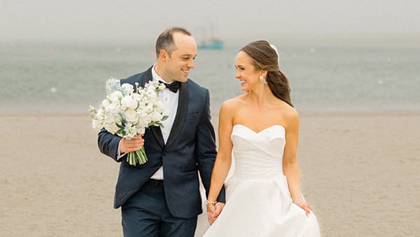 Laura Savage and Andrew Czuchra walk along the beach holding hands on their wedding day