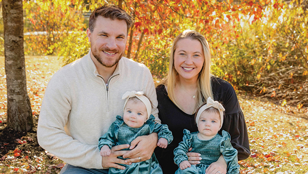 Julia (Gonsalves) Mann and Chris Mann hold their two daughters on a bench on a fall day