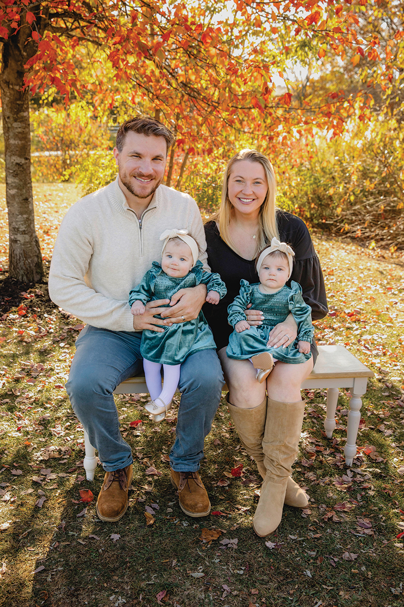 Julia (Gonsalves) Mann and Chris Mann hold their two daughters on a bench on a fall day