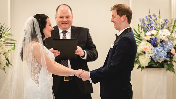 Meghan and Connor Aikens-Kinney hold hands while Justin Kile presides on a wedding alter